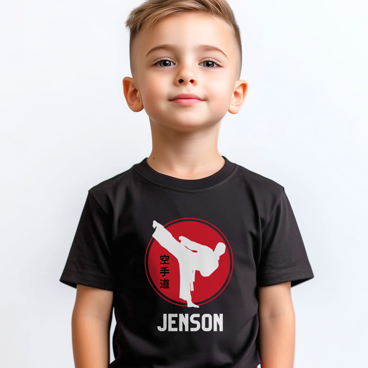 Young boy wearing a black personalised karate T-shirt featuring a white martial artist silhouette performing a high kick inside a red circle with Japanese kanji text, and the custom name “Jenson” printed underneath.
