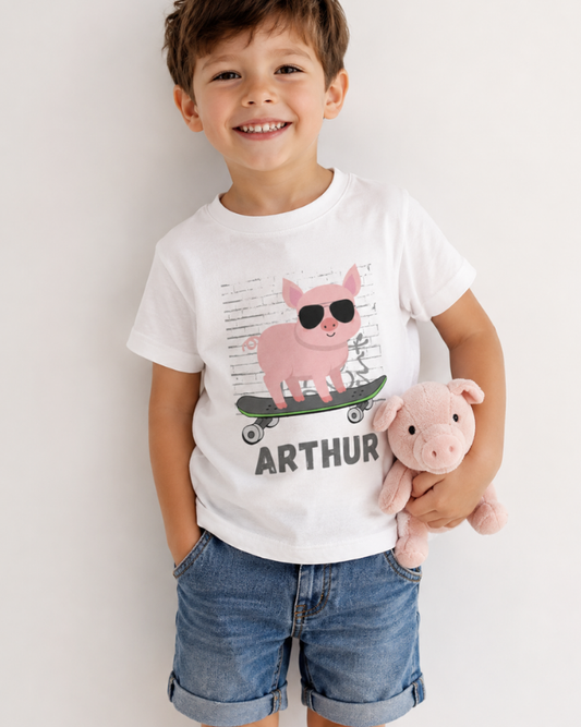 Boy wearing personalised pig skateboard T-shirt with denim shorts and pink pig plush toy