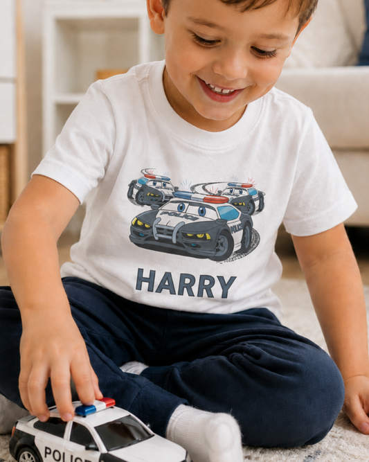 Little boy wearing a white t-shirt with a police car design and name 'Harry', holding a toy police car.
