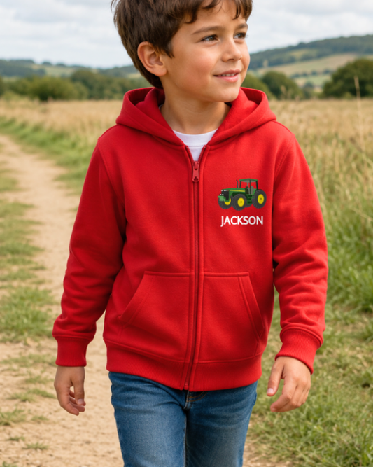 Young boy wearing a red hoodie with a tractor design and 'Jackson' text, walking through a field.