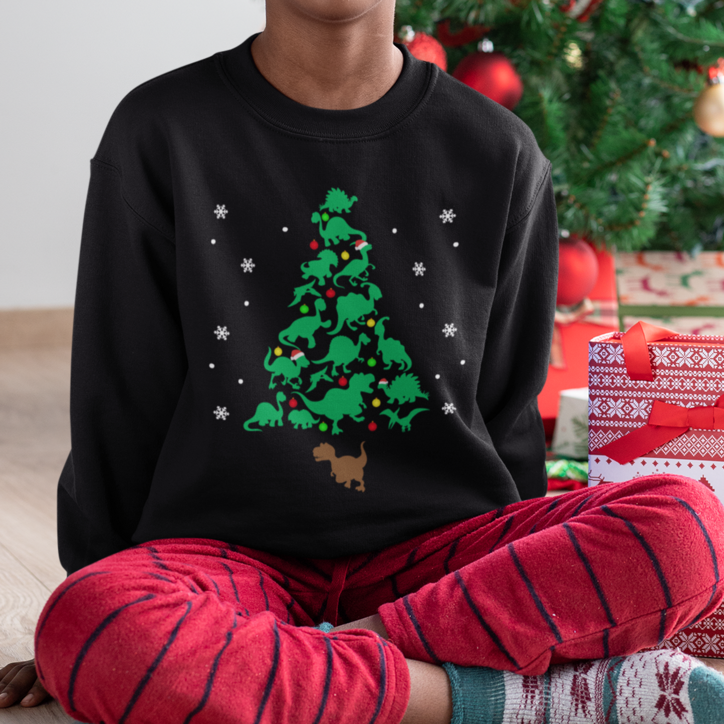 A young boy wearing a black Christmas sweatshirt with dinosaur-shaped tree design, decorated with ornaments and snowflakes