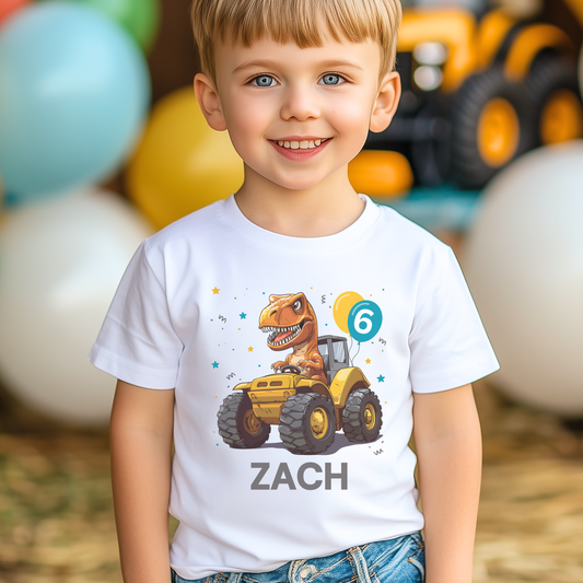 A child wearing a white T-shirt with a colorful print of a dinosaur driving a tractor, with the name 'ZACH' printed on the front.