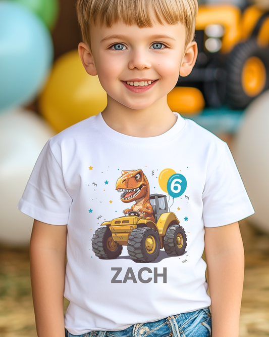 A child wearing a white T-shirt with a colourful print of a dinosaur driving a tractor, with birthday balloons and the name 'ZACH' printed on the front.
