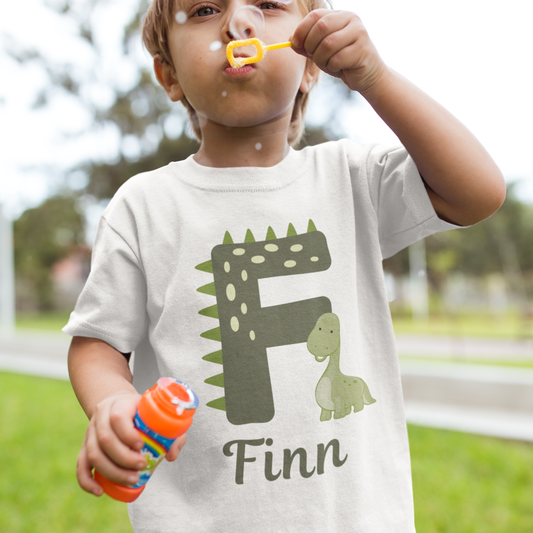Little boy blowing bubbles wearing a shirt with a dinosaur design and the name 'Finn'.