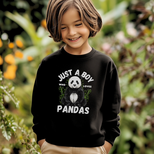 Smiling young boy wearing a black sweatshirt with a cute panda graphic and the slogan "Just a Boy Who Loves Pandas," standing outdoors in a leafy garden setting.