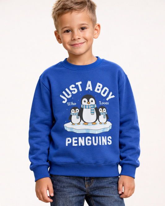 Smiling boy wearing a royal blue “Just a Boy Who Loves Penguins” jumper with dark jeans against a plain light studio background.
