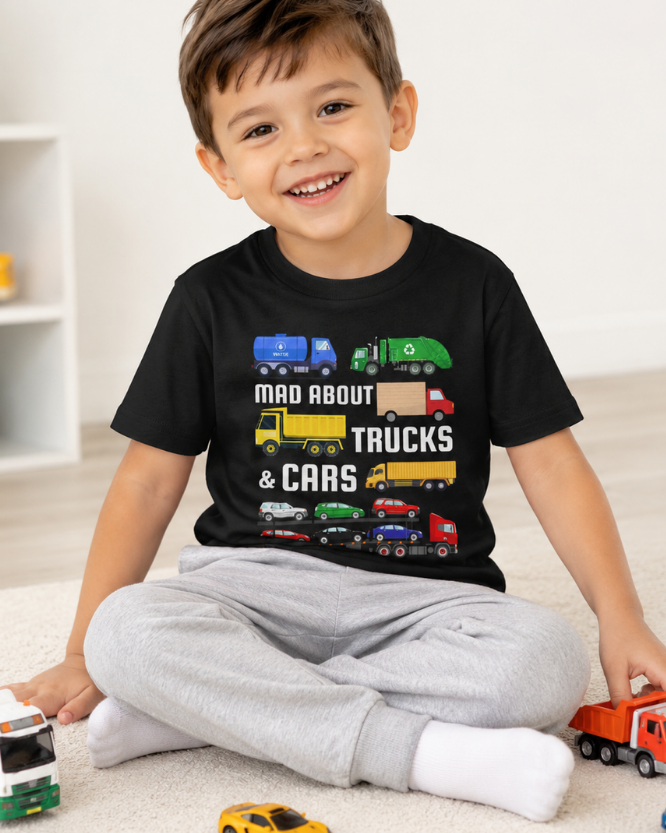 Young boy wearing a black t-shirt with trucks and car graphics, sitting on the floor with toy vehicles.