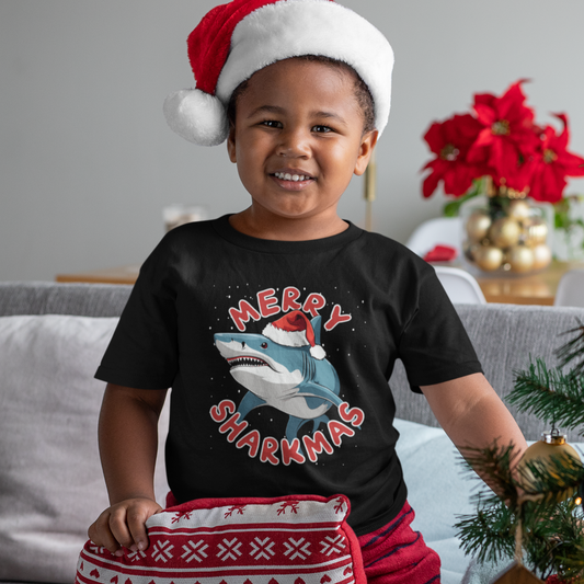 Child wearing a black t-shirt with a shark graphic and 'Merry Sharkmas' text, sitting on a couch.