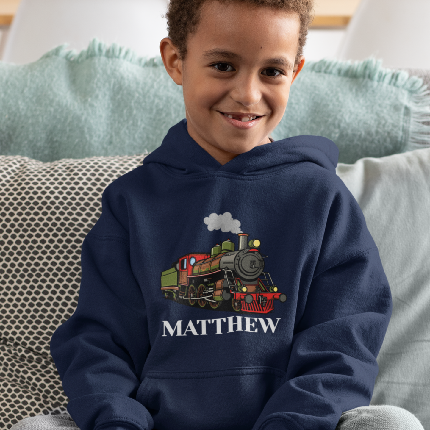 Smiling young boy wearing a navy hoodie with a colourful steam train graphic and the custom name “Matthew” printed underneath on the front.