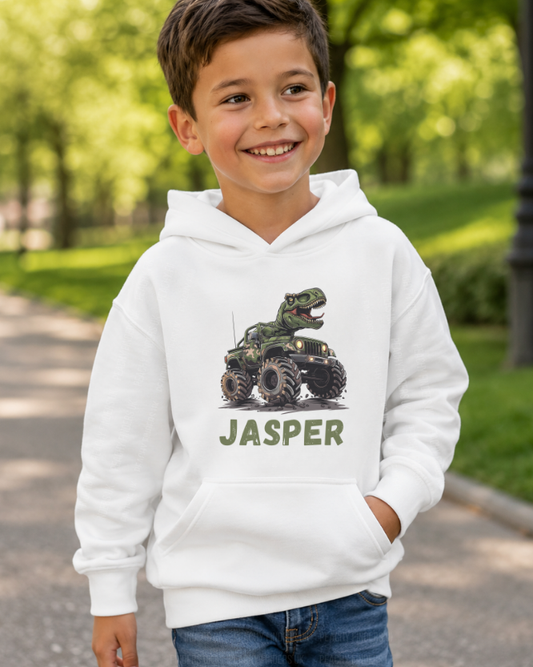 Smiling boy wearing white personalised hoodie with T-Rex riding camo monster truck and name Jasper printed on front - park background.