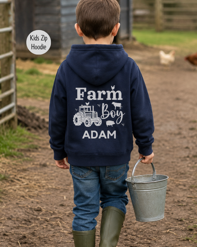 Young boy wearing personalised navy Farm Boy hoodie with tractor back print carrying bucket in farmyard scene.