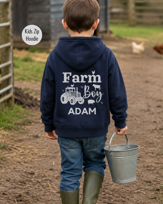 Young boy wearing personalised navy Farm Boy hoodie with tractor back print carrying bucket in farmyard scene.