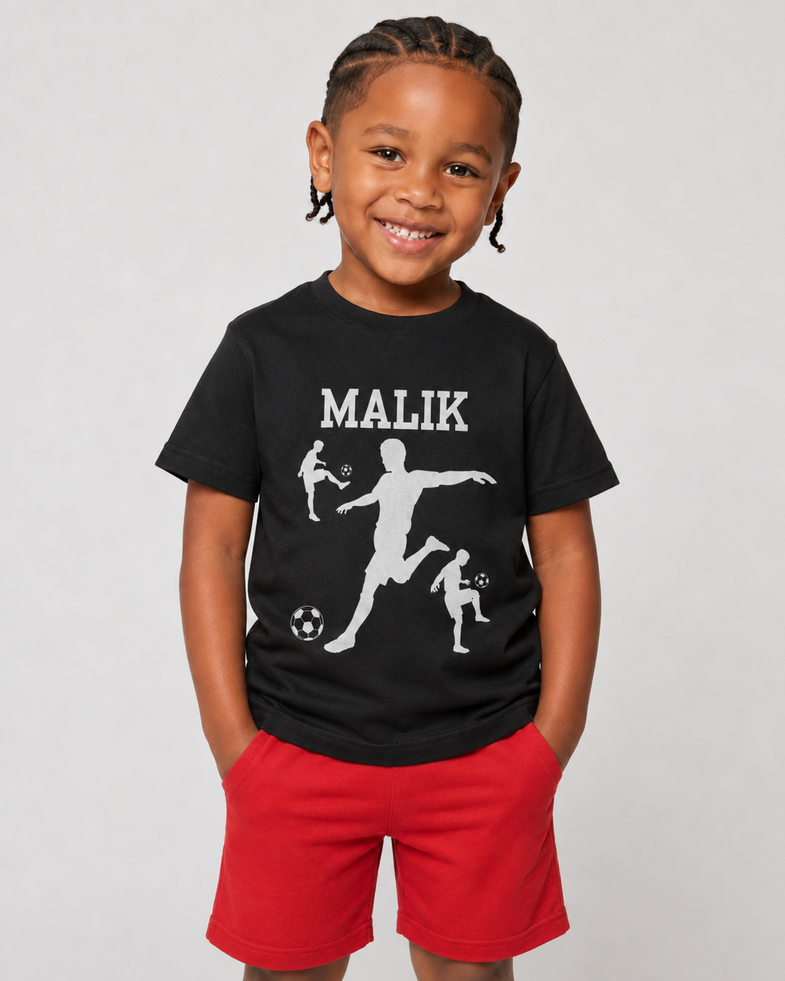 Smiling young boy wearing a black personalised football T-shirt with white player silhouette design and red shorts.