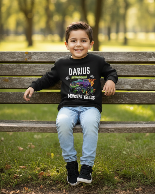 Smiling boy sitting on park bench wearing personalised monster truck sweatshirt with custom name Darius and denim jeans.