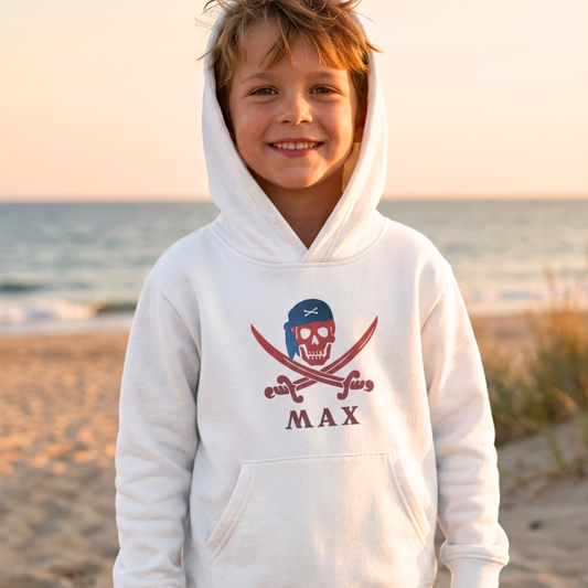 Boy wearing white personalised pirate skull and crossbones hoodie with name Max at the beach