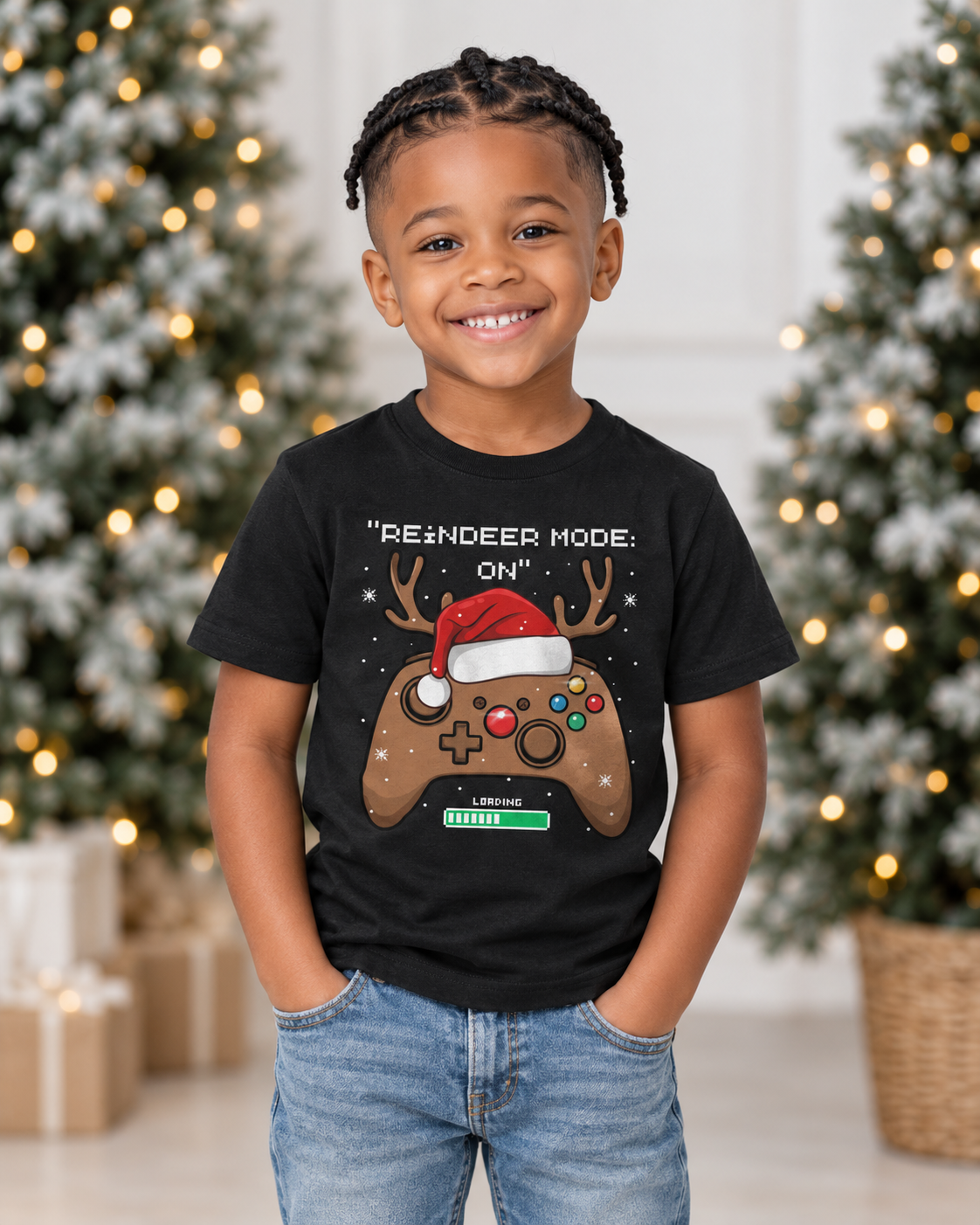 Smiling six-year-old boy wearing a black Reindeer Mode On gaming Christmas T-shirt with jeans beside festive trees.