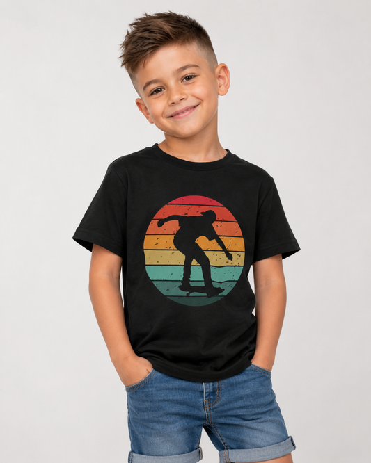 A young boy smiling and posing in a black t-shirt with a retro circular graphic of a skateboarder silhouette against a sunset gradient, paired with blue denim shorts, set against a plain light grey background.