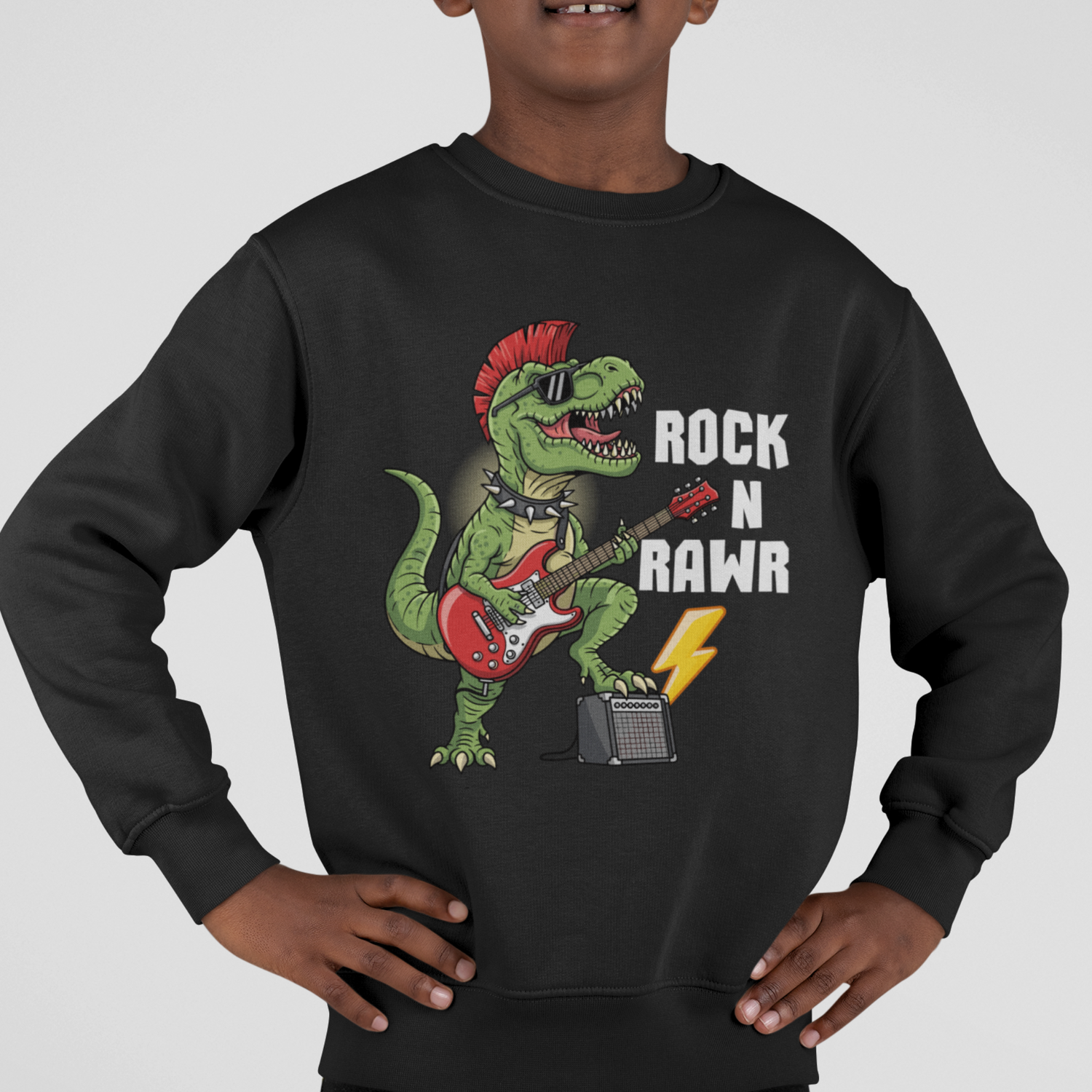 Boy models a black sweatshirt featuring a fun ‘Rock N Rawr’ dinosaur playing a guitar with amp and lighting bolt.