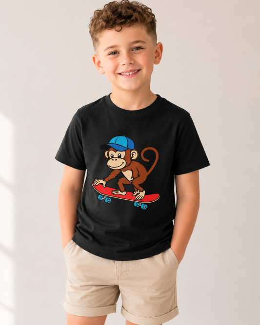 Young boy wearing a black skateboard monkey graphic T-shirt and beige shorts in a studio setting, smiling with hands in pockets.