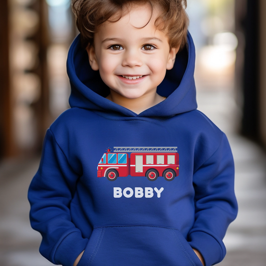 A little boy wearing a blue hoodie with a printed fire engine design and personalised name in white 