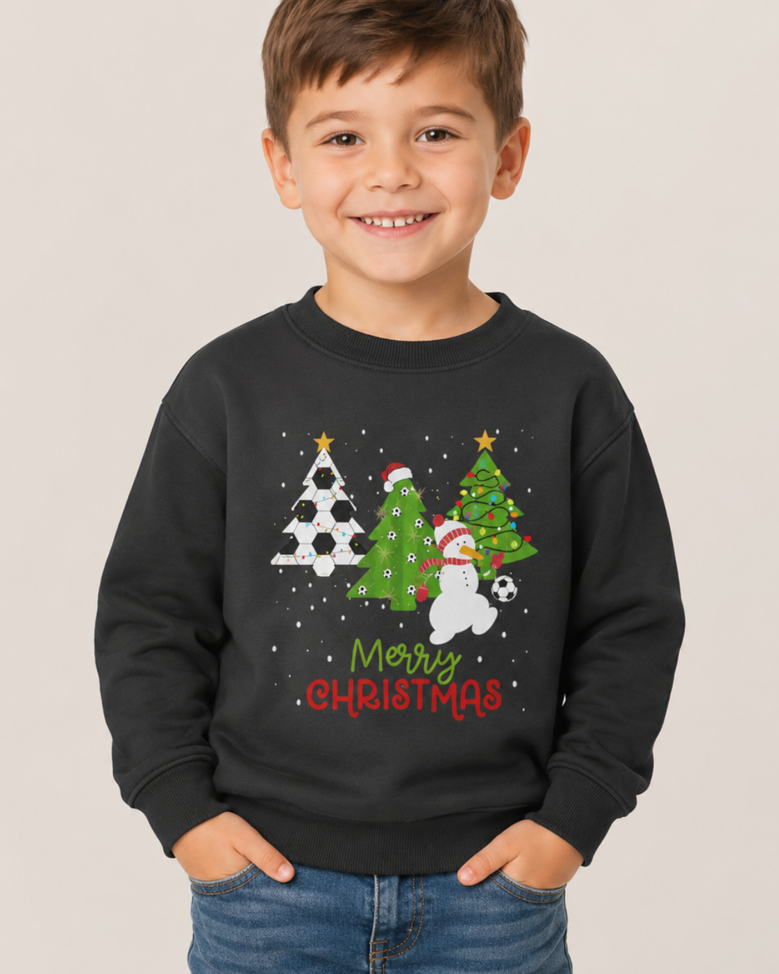 Smiling 5-year-old boy wearing a black football Christmas sweatshirt with festive trees and snowman design, styled with denim jeans in a studio.