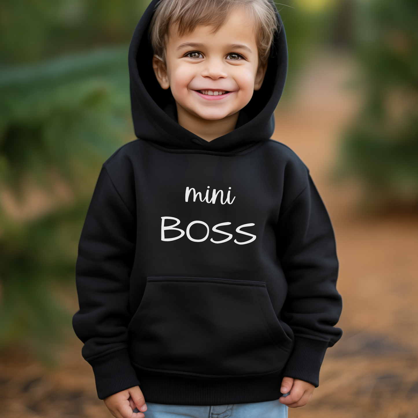 A little boy wearing a black hoodie with the white printed words saying "mini boss"