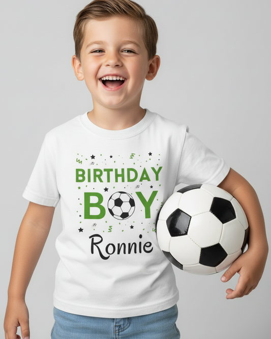 Smiling young boy wearing a white personalised “Birthday Boy” football t-shirt with the name Ronnie, holding a black and white soccer ball, studio background