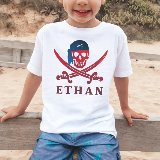 A young boy smiles, wearing a white t-shirt with a pirate skull and cross swords graphic and the name "Ethan" printed below.