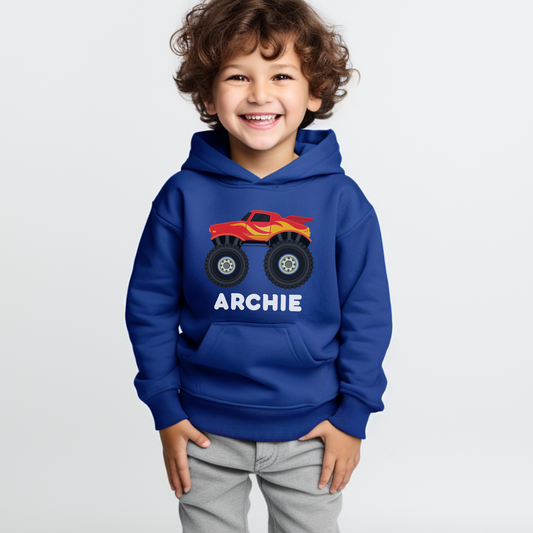 A little boy wearing a blue hoodie with a printed monster truck graphic and personalised name in white