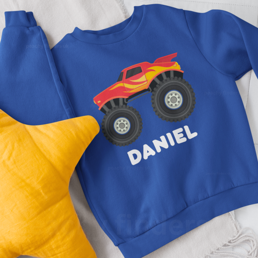 Kids royal blue jumper featuring a red and yellow monster truck graphic with large tyres and custom name printed below the design.