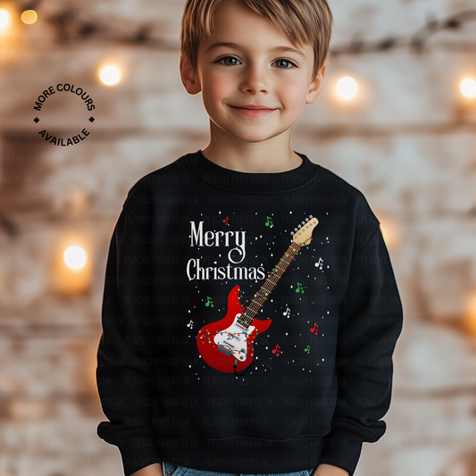 Young boy wears black sweatshirt with a red electric guitar tangled in fairy lights, festive musical notes design and 'Merry Christmas' text
