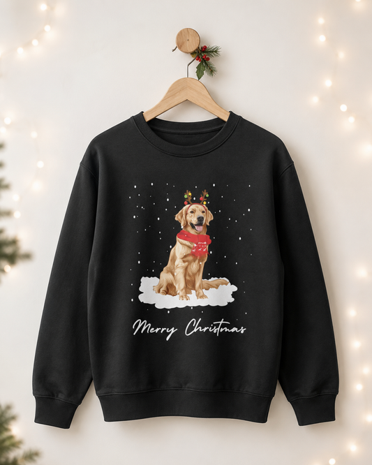 Adults black crewneck sweatshirt hanging on a wooden hanger against a warm, softly lit background with string lights. The sweatshirt features a graphic of a golden retriever wearing a red scarf and reindeer antlers, sitting in a snowy white cloud, with 'Merry Christmas' written below.