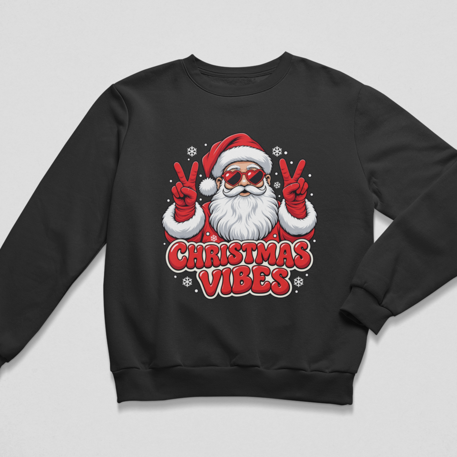Flat lay of a kids black Christmas crewneck sweatshirt featuring a graphic of Santa Claus wearing heart-shaped sunglasses and red mittens throwing up peace signs, surrounded by snowflakes and the red text "CHRISTMAS VIBES".