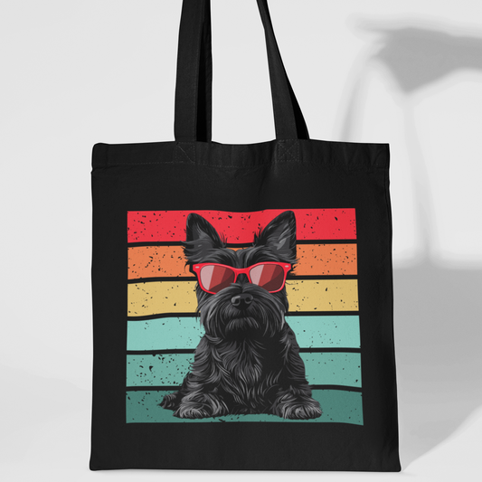 A black tote bag with black handles. The main design on the bag is a digitally printed image of a black Scottish Terrier dog sitting and wearing bright red rectangular sunglasses. Behind the dog is a horizontal striped retro design in red, orange, yellow, and teal, with a slightly distressed or faded texture.