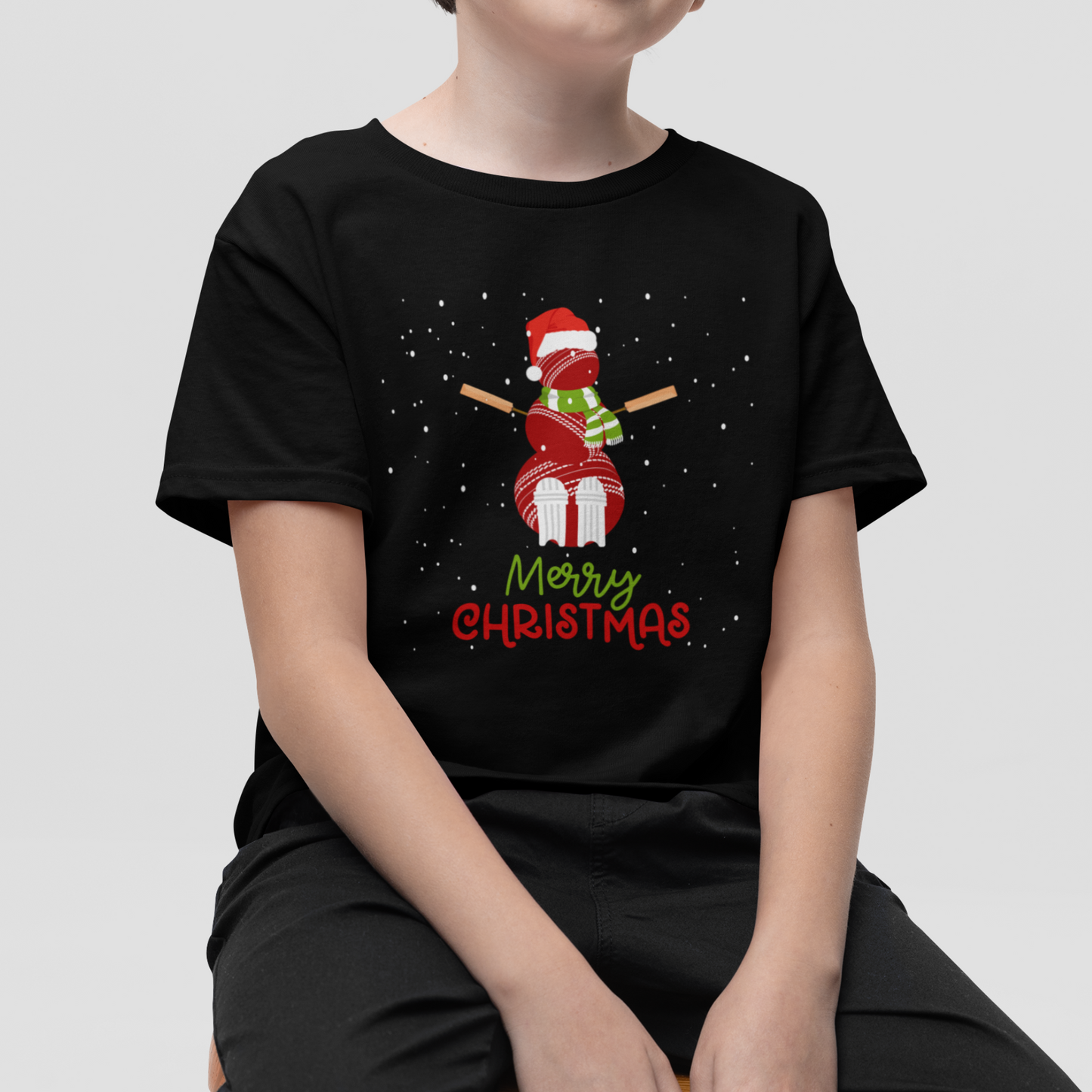 A boy wears a black short-sleeve t-shirt with a cricket ball snowman wearing a Santa hat with falling snow.