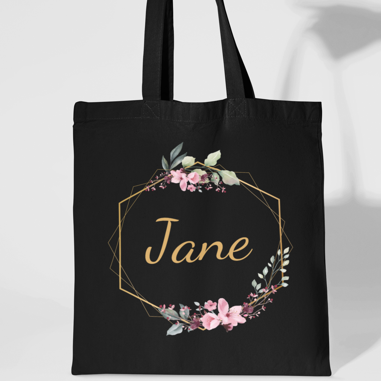 Black cotton tote bag with floral gold hexagon frame and personalised name “Jane” in gold script.