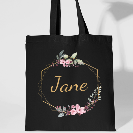 Black cotton tote bag with floral gold hexagon frame and personalised name “Jane” in gold script.
