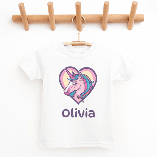 Girls white cotton t-shirt featuring a unicorn inside a pink and purple heart with the name “Olivia” printed below, styled on a wooden hanger.