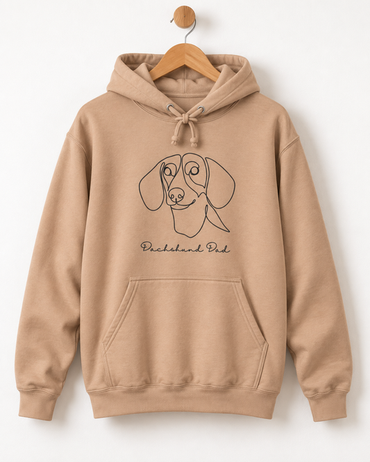 Nude (dark beige) coloured adult hoodie on a wooden hanger with a black dachshund line-art portrait and handwritten “Dachshund Dad” design below it.