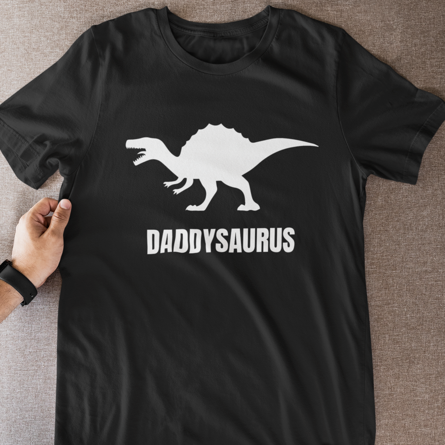 Flat lay of a black Daddysaurus T-shirt with white dinosaur graphic and bold slogan across the chest.