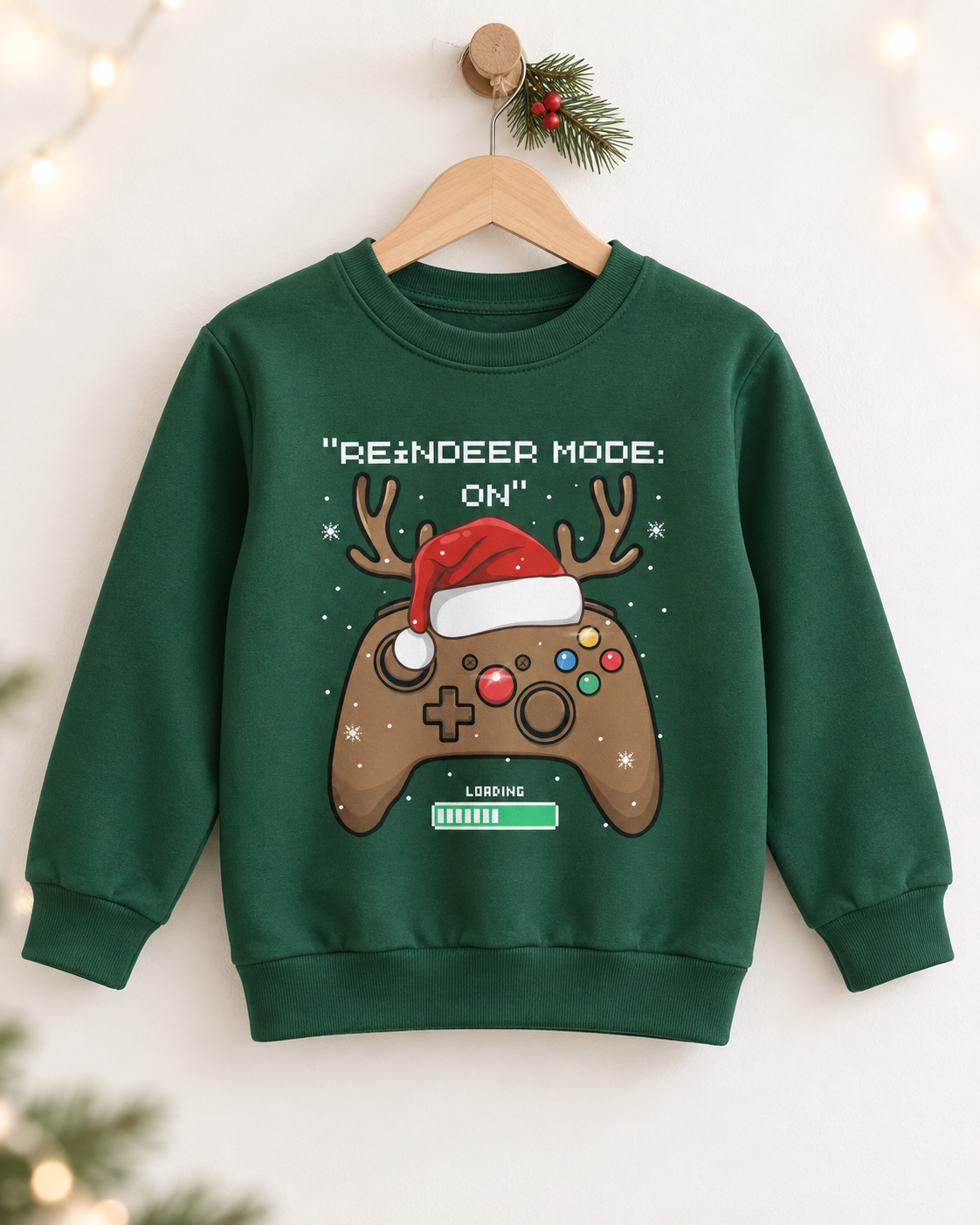 Children’s dark-green festive gamer sweatshirt on a wooden hanger with holly and warm fairy lights.