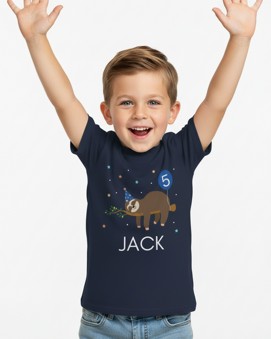 Excited boy wearing navy personalised 5th birthday sloth t-shirt with balloon number 5 and name JACK, studio image.