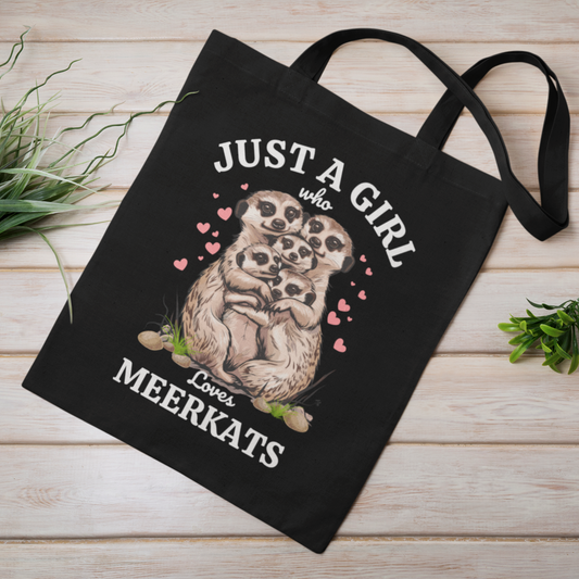 A black cotton tote bag with an illustration of meerkats and the text 'JUST A GIRL WHO LOVES MEERKATS' printed on it, along with various heart and floral designs.