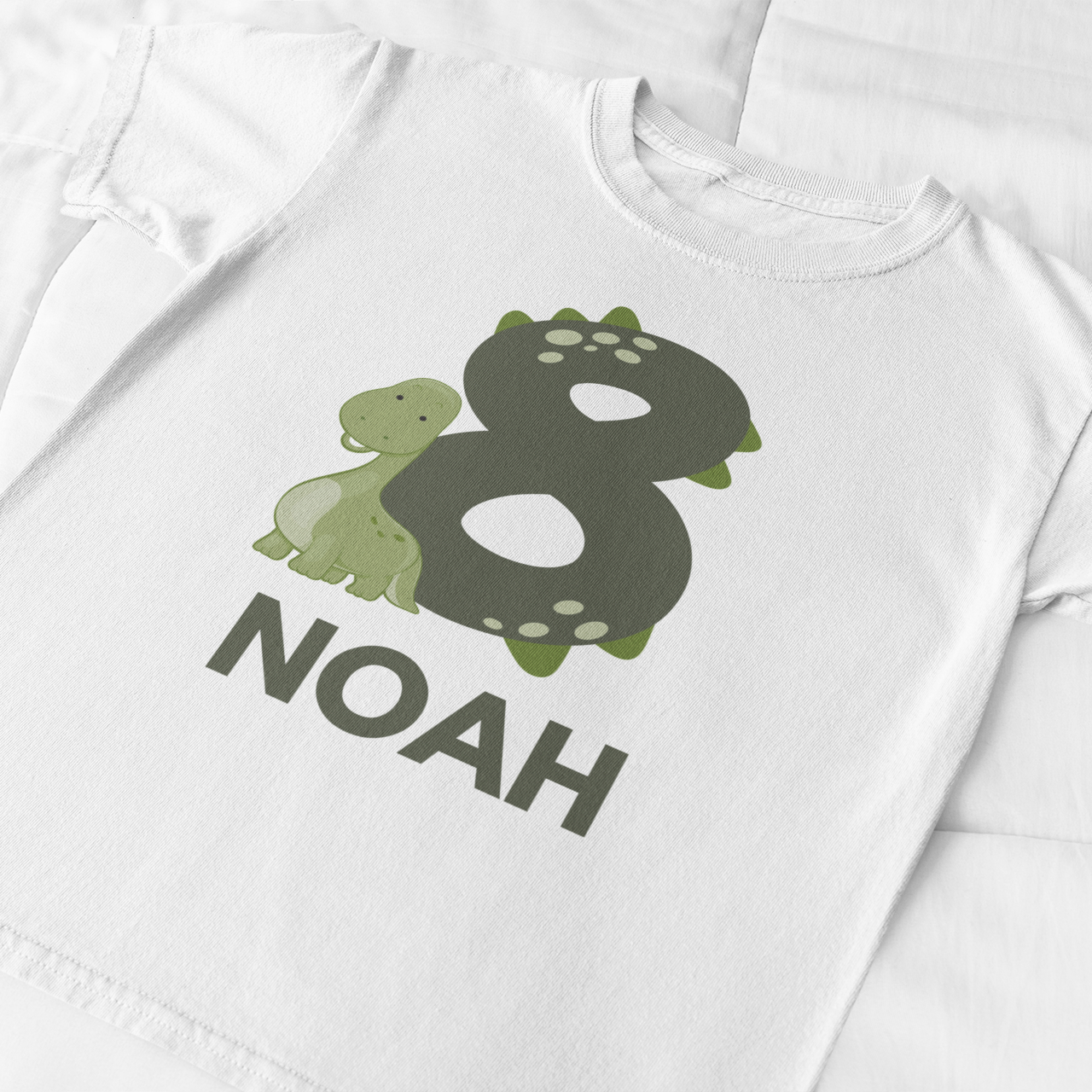 Personalised 8th birthday dinosaur t-shirt with name Noah, minimal green number eight birthday shirt flat lay on white fabric