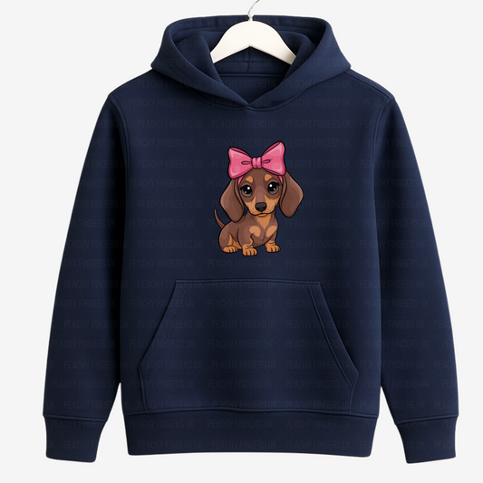 Kids navy hoodie with a cartoon dachshund wearing a pink bow graphic on a wooden hanger