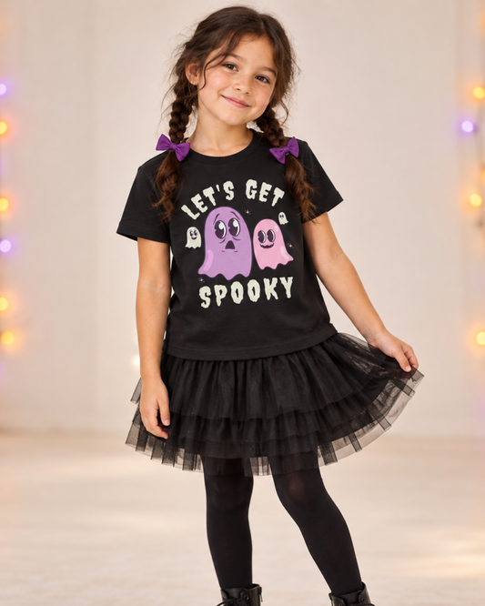 Girl wearing a black Halloween T-shirt with pink and purple ghosts and “Let’s Get Spooky” lettering.