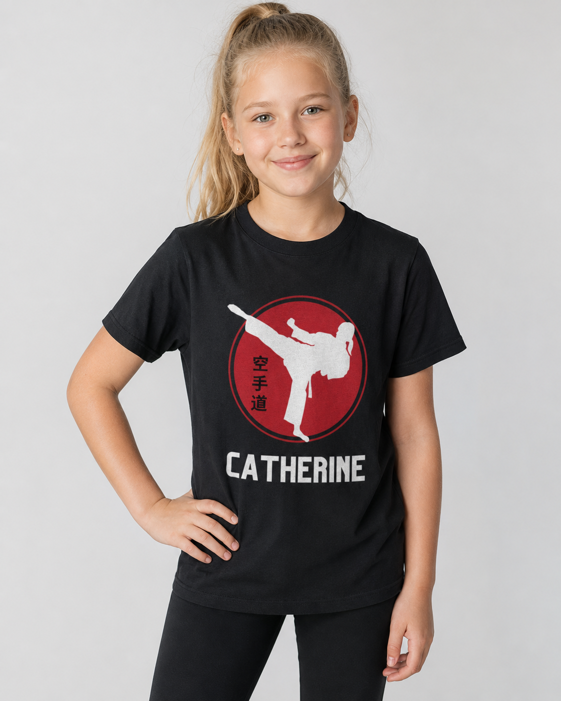 Young girl wearing a personalised black karate T-shirt with a female martial arts kick graphic and custom name in a studio setting.