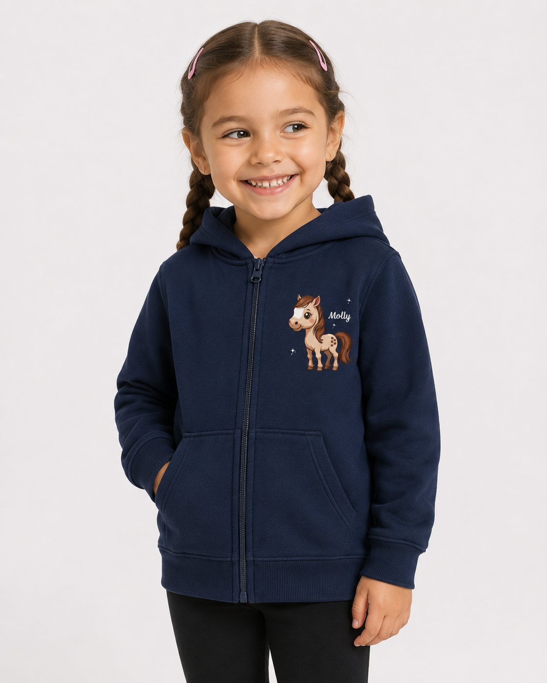 A young girl with braided hair smiling while wearing a navy blue zip-up hoodie with a cartoon horse graphic on the chest, paired with black leggings, against a light grey background.