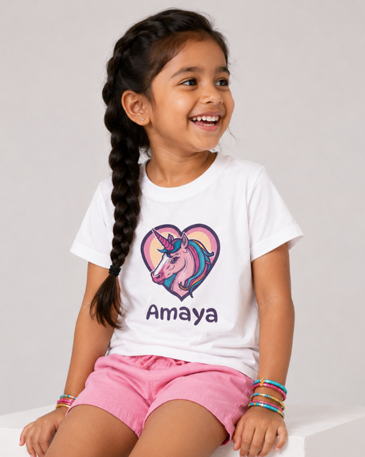 Girl wearing personalised unicorn “Amaya” white T-shirt with pink shorts and colourful bracelets.