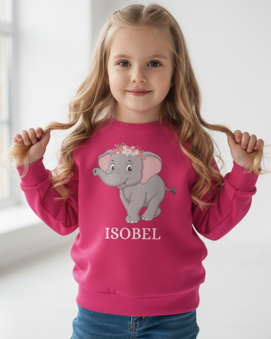 Young girl modelling pink custom elephant jumper with floral crown elephant graphic and “Isobel” name print, light studio background.
